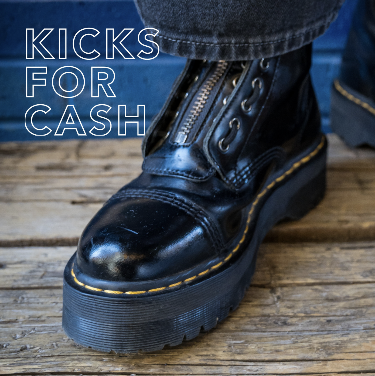Close-up image of a black leather platform combat boot with a front zipper and yellow stitching, worn with dark jeans, standing on a wooden floor. White outlined text on the left reads “KICKS FOR CASH.”